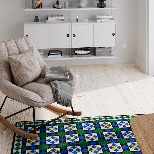 Ambiente com tapete de arraiolos colorido, uma poltrona e um armário com decoração.